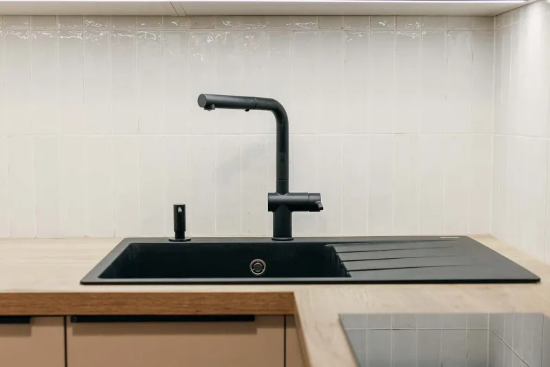 Kuchyňský dřez s černou baterií a světlým obkladem