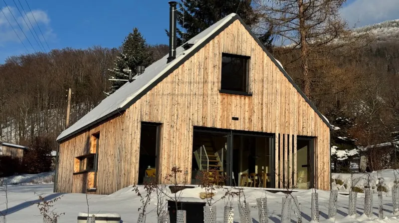 Dřevěný domek s velkými okny v zasněženém údolí